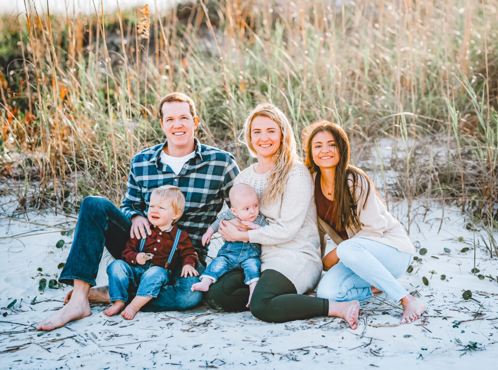 young family poses with au pair at the beach